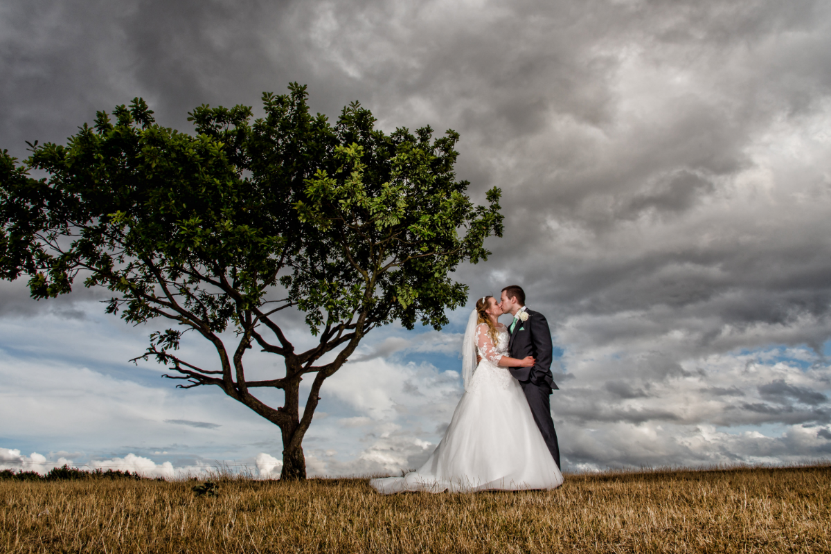 bride and groom stood next to a tree kissing.